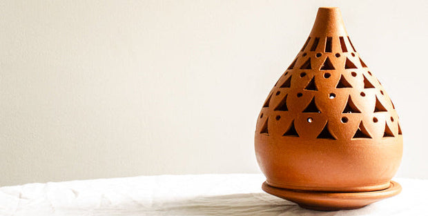 Terracotta oil burner with geometric design on a white surface