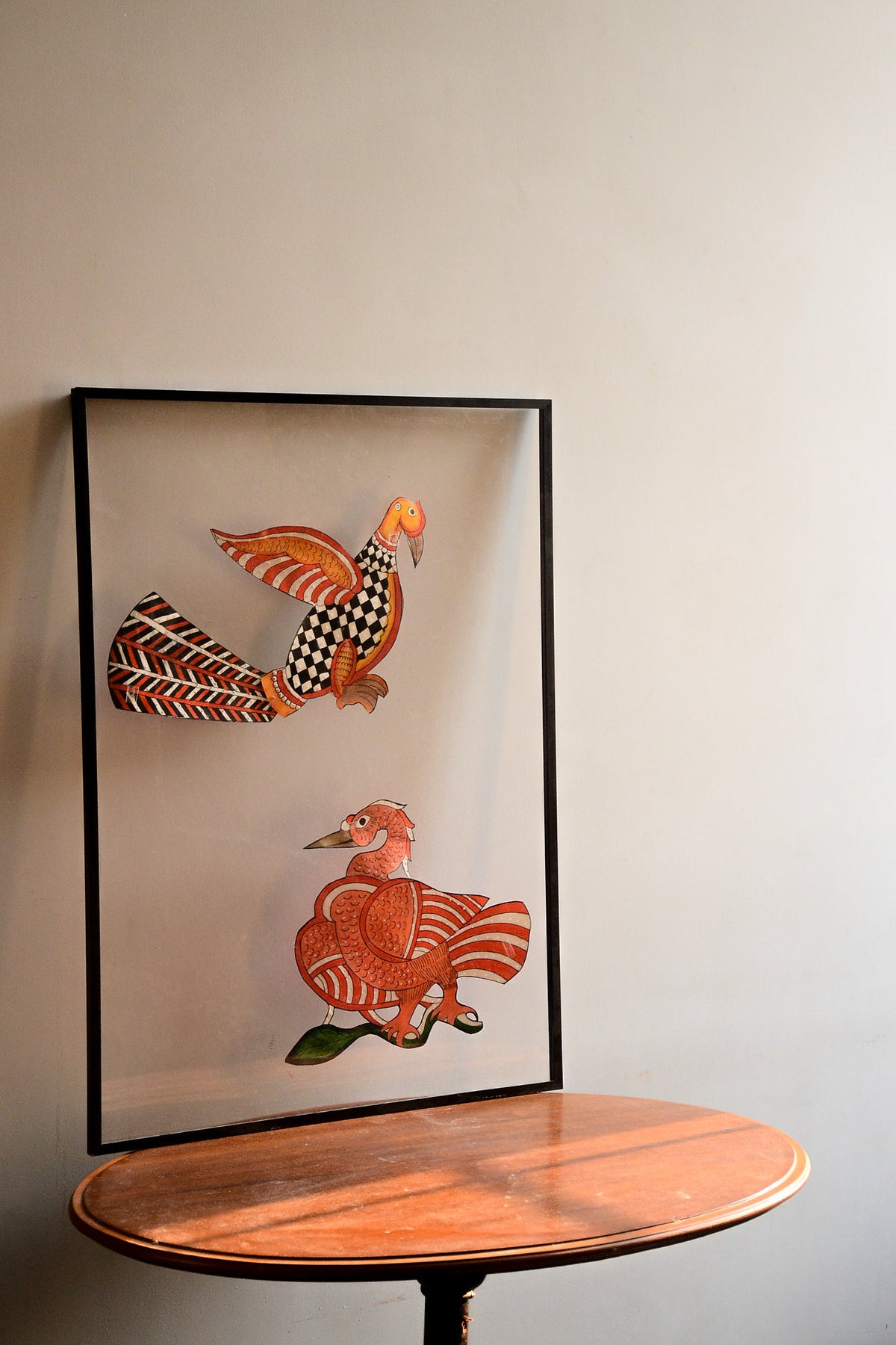 Tholu Bommalata puppets - Hamsa and checkered bird pair in vermilion, black and white, shown mounted for display on a round wooden table