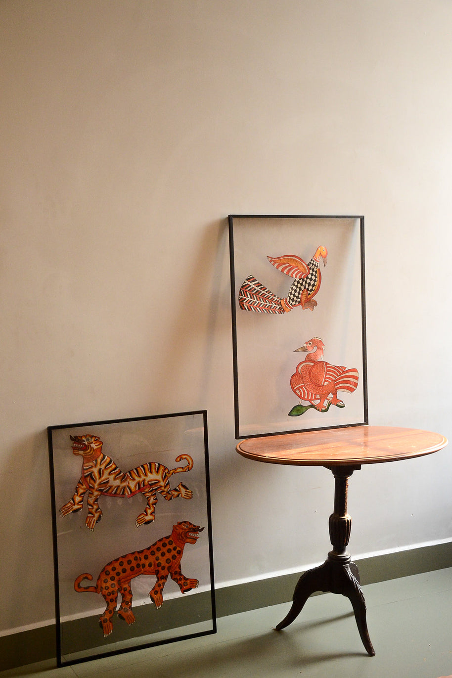 Two pairs of Tholu Bommalata leather puppets - tiger and leopard, Hamsa and checkered bird - shown mounted for display beside a pedestal table