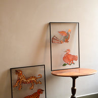 Two pairs of Tholu Bommalata leather puppets - tiger and leopard, Hamsa and checkered bird - shown mounted for display beside a pedestal table