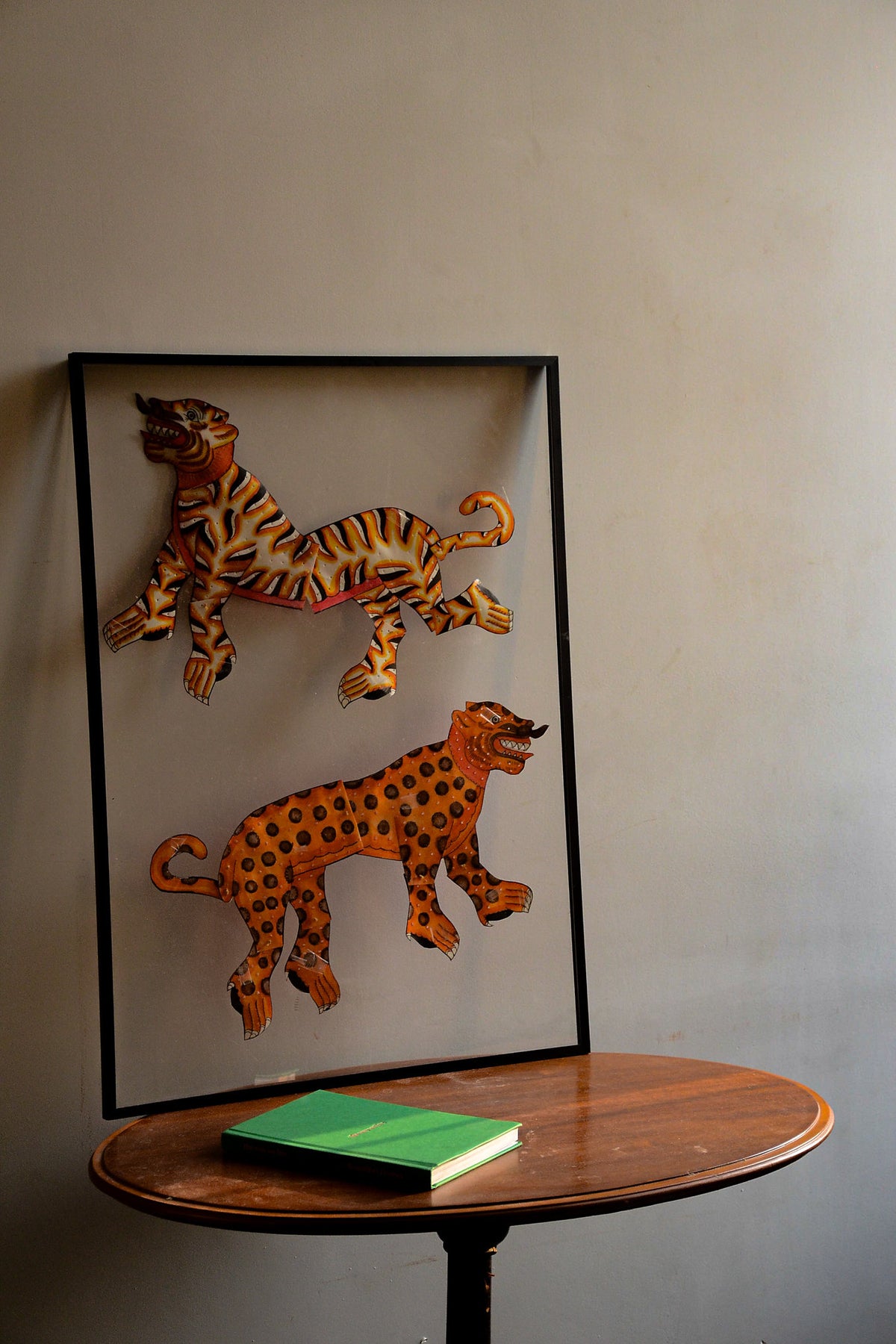 Tholu Bommalata leather puppets - tiger and leopard pair, hand-cut and hand-painted, shown mounted for display above a wooden pedestal table